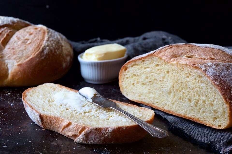 Loaf of sourdough bread on a cutting board, sliced, with a crock of butter.